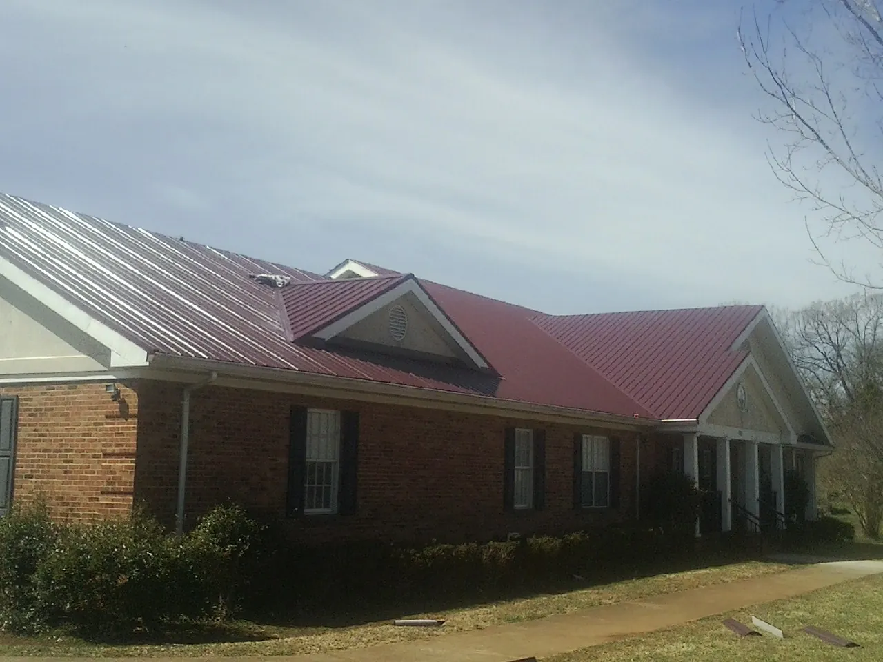 Red metal roof with gabled entries on a long brick building, from a Hail Damage Roof Repair job in Oak Ridge