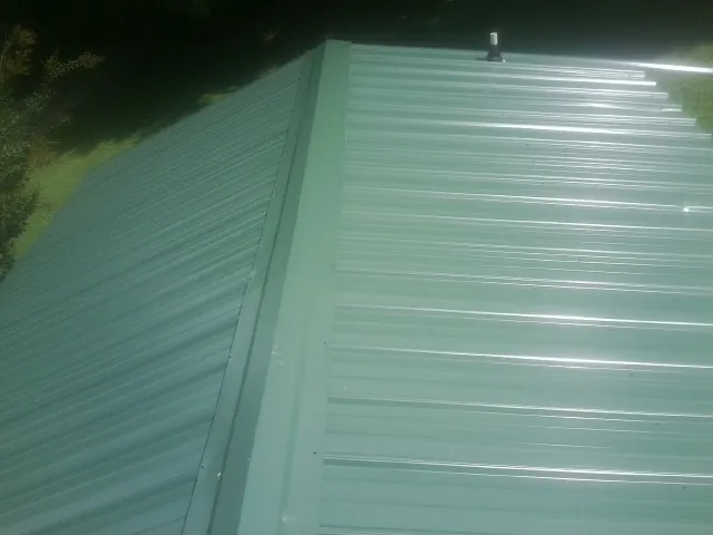 New green metal panels meeting at the ridge of a roof — Flat Roof Repair work by our crew in Oak Ridge